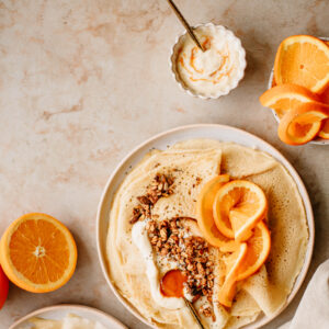 Naleśniki z jogurtem, granolą i plasterkami pomarańczy sfotografowane na jasnym, neutralnym tle fotograficznym MBackdrops
